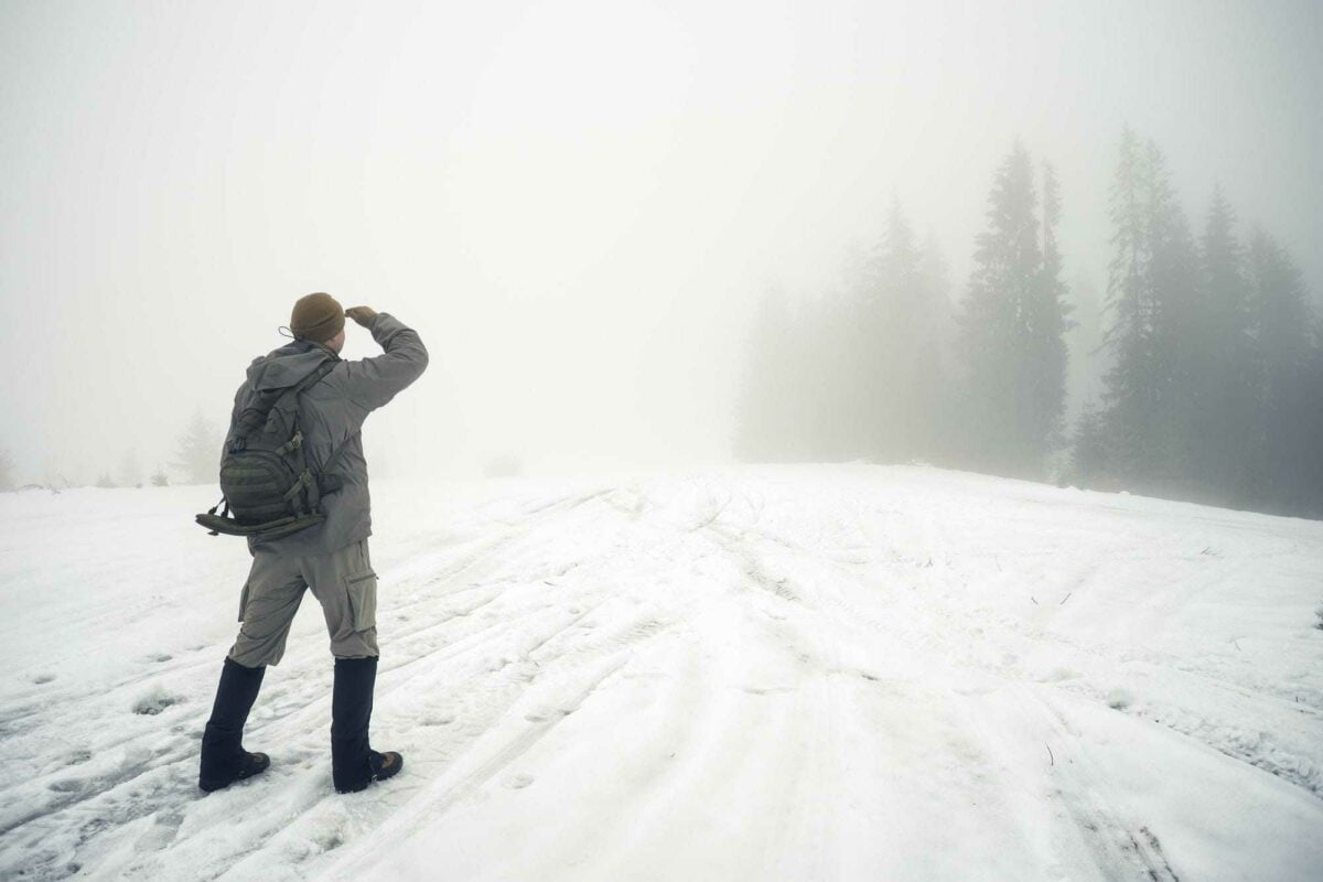 Man with backpack in the winter mountains peers into the foggy d