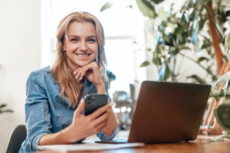 glad blond haired woman sitting at table with laptop and mobilephone 1