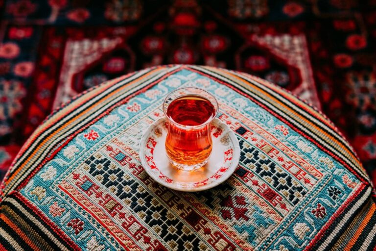 Kleines Glas mit schwarzem Tee auf Tischdecke mit orientalischem Muster