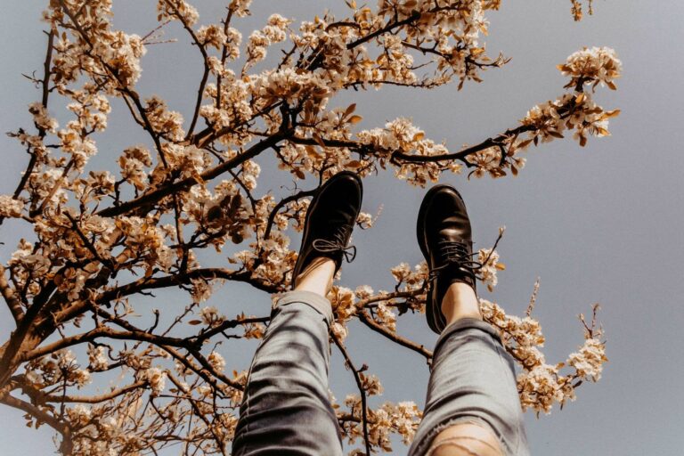 2 Beine ragen in den blauen Himmel, dahinter ein blühender Kirschbaum