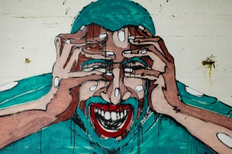 Angst am Arbeitsplatz: Das Bild zeigt Streetart. An einer Wand ist eine Person im türkisen Kapuzenpulli. Es ist nur der Oberkörper zu sehen. Die Person verzeiht angsterfüllt ihren Mund und hält sich die Hände vor die Augen.