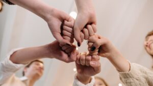 Mehrere Personen legen ihre Fäuste in der Mitte zusammen – Symbol für Teamgeist, Zusammenhalt und gemeinsames Leadership.